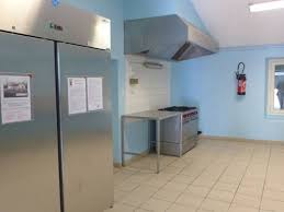 Cuisine professionnelle avec réfrigérateur, plan de travail, hotte, et extincteur mural.