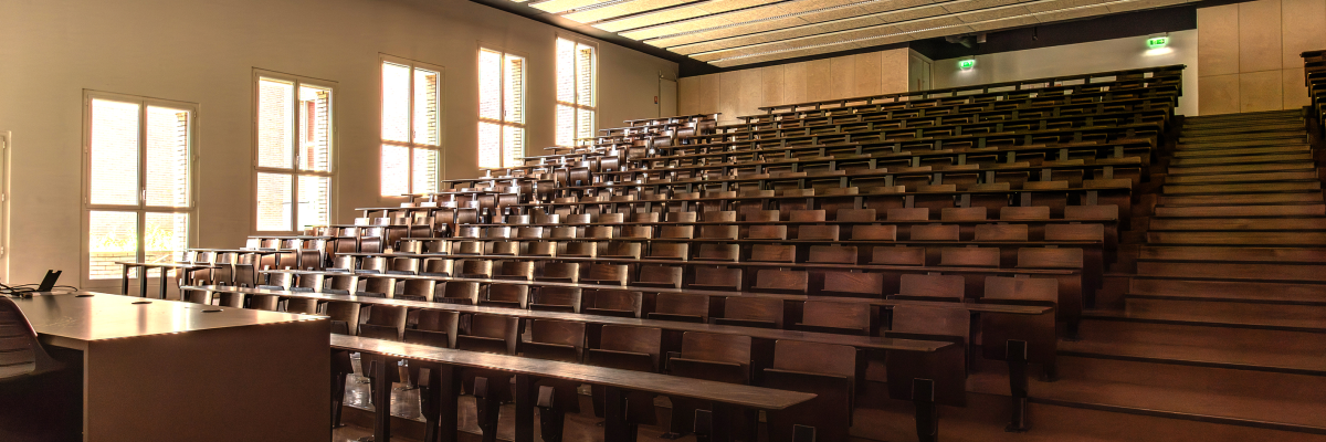 Amphithéâtre avec rangées de sièges, tables, estrade et projecteur.