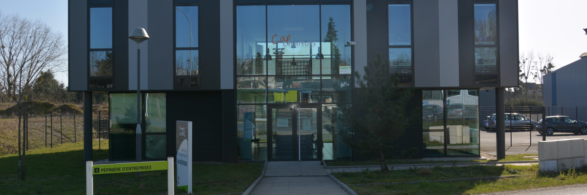 Bâtiment moderne avec façade vitrée, entrée principale, allée et panneaux de signalisation.