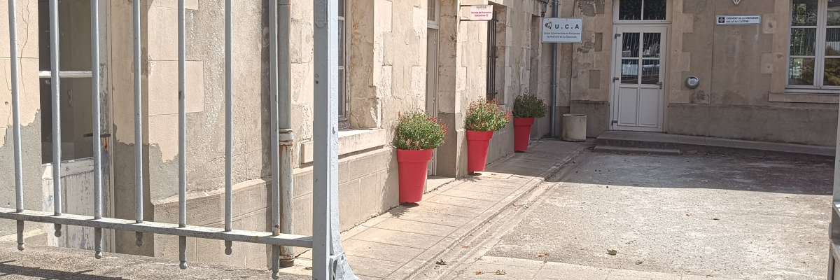 Cour intérieure avec bâtiments, portes, fenêtres, pots de fleurs et bancs.