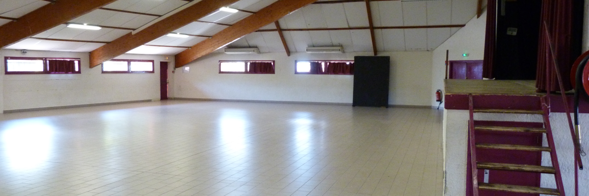 Salle spacieuse avec sol carrelé, escaliers et grandes fenêtres.