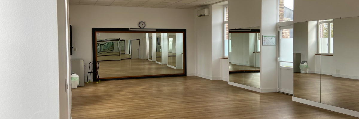 Salle avec miroirs, sol en bois, climatiseur, portes vitrées.