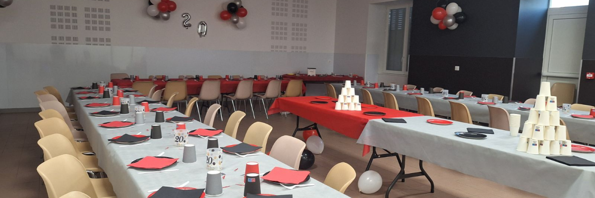 Salle avec tables, chaises, nappes, verres, couverts et décorations.