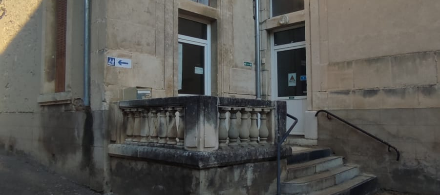 Bâtiment avec entrée, escalier, et poubelle.