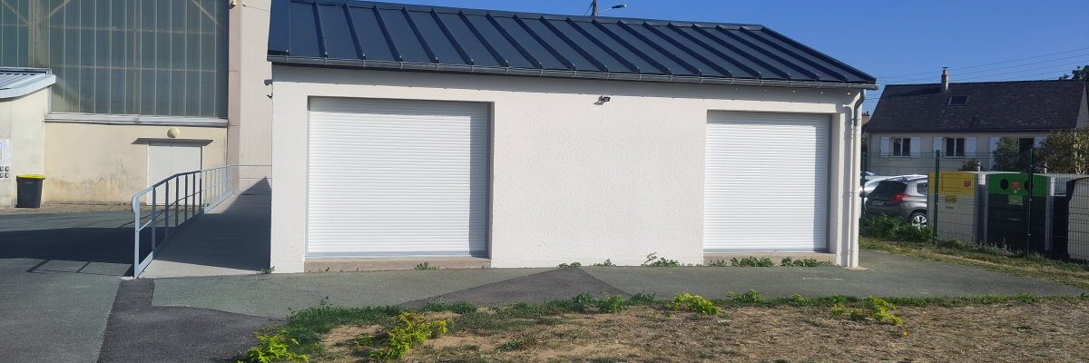 Bâtiment avec deux portes de garage blanches, toit plat, rampes d'accès et terrain herbeux.