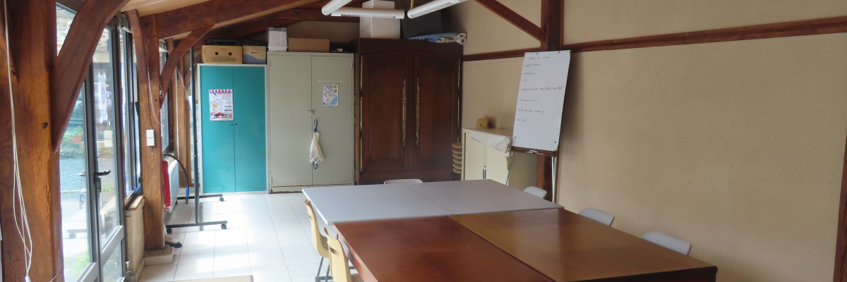 Salle avec tables, chaises, tableau blanc, frigo, étagères et fenêtres.