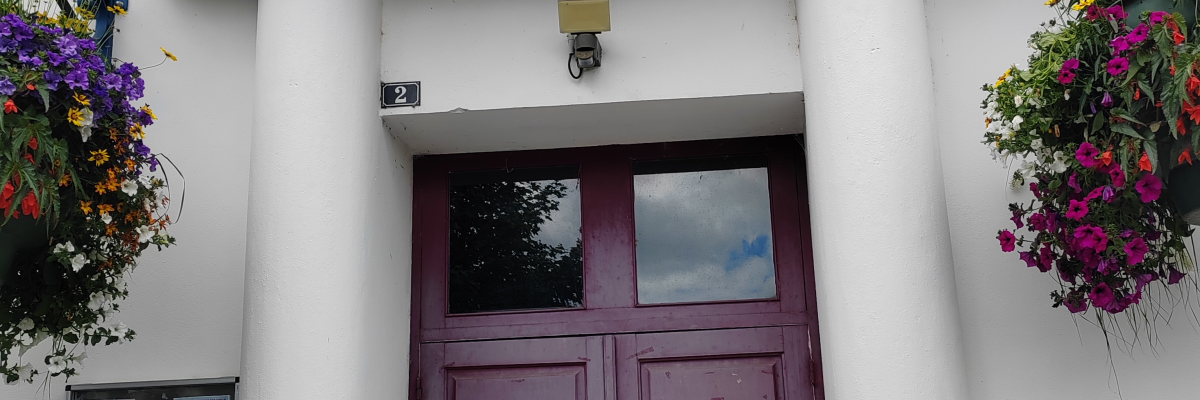Façade avec porte, colonnes, enseigne et jardinières suspendues.