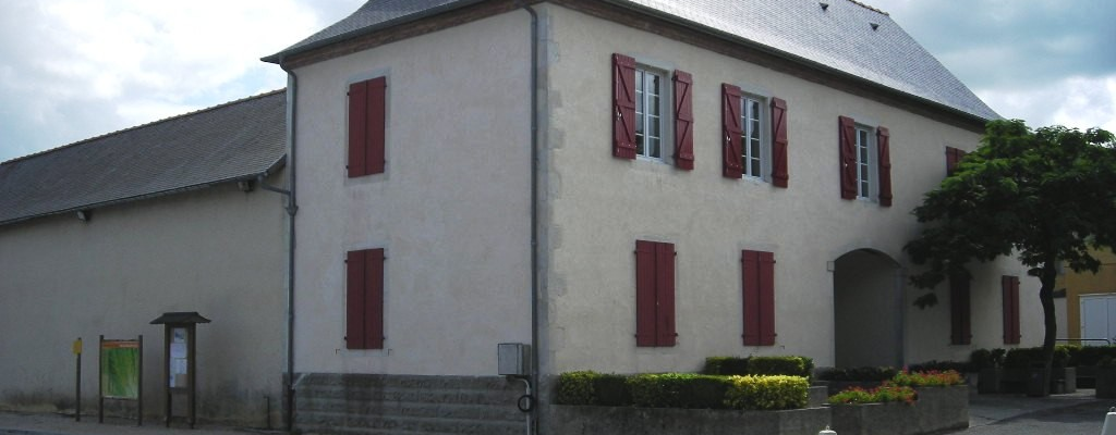 Maison blanche à deux étages avec volets rouges, toit en pente, et une entrée principale avec une arche. Arbre à feuilles vertes à droite. Panneaux d'affichage et parcmètre devant la maison. Route pavée.