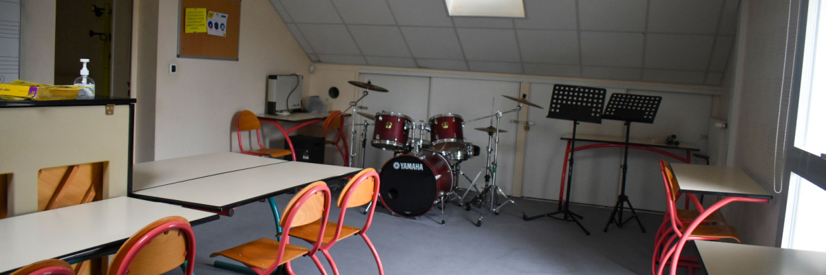 Salle de musique avec batterie, pupitres, tables et chaises.