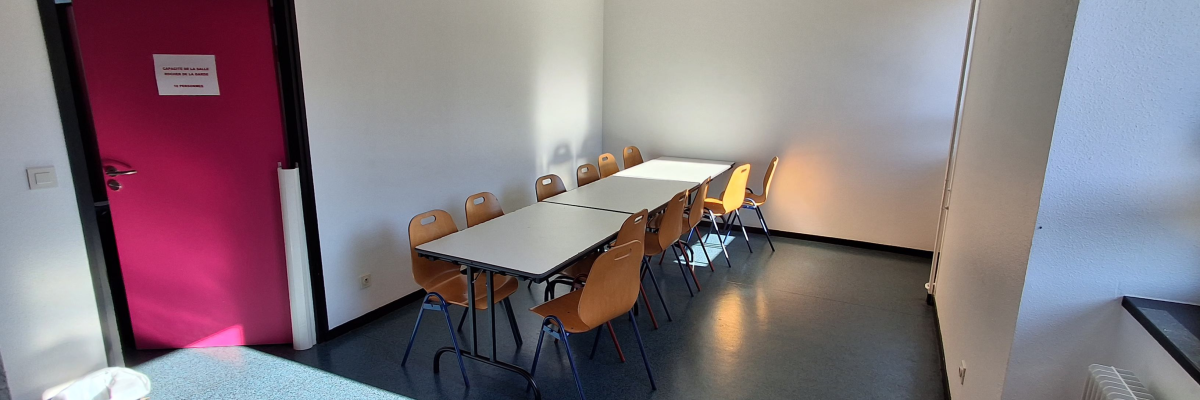 Salle avec tables, chaises, porte rouge, radiateur et poubelle.