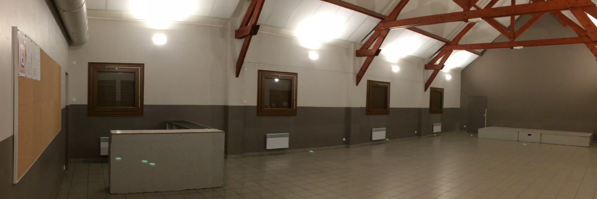 Salle vide avec poutres apparentes, sol carrelé, comptoir, fenêtres et portes.