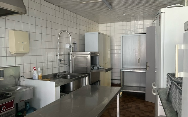 Cuisine avec plans de travail en acier inoxydable, évier, robinet, distributeur de savon, réfrigérateur et plaques de cuisson.