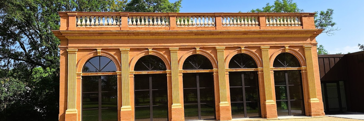 Bâtiment avec façade arcades, graviers et gazon.