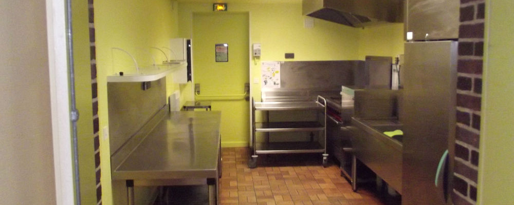 Cuisine équipée avec plans de travail, éviers, réfrigérateur, plaque de cuisson et hotte.