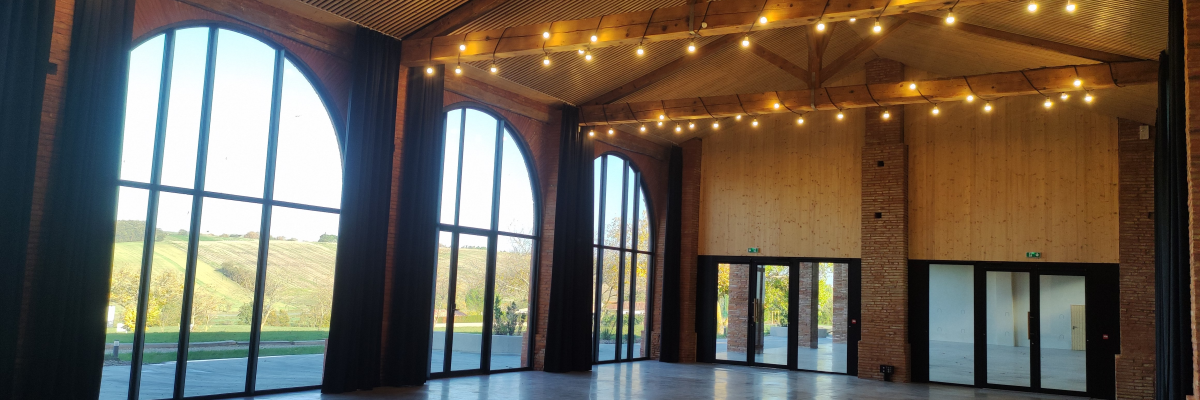 Salle spacieuse avec grandes fenêtres, portes, éclairage suspendu et plafond en bois.