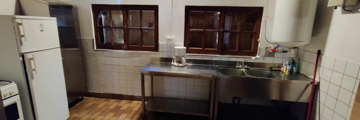 Cuisine avec réfrigérateur, four, plan de travail, évier et ballon d'eau chaude.