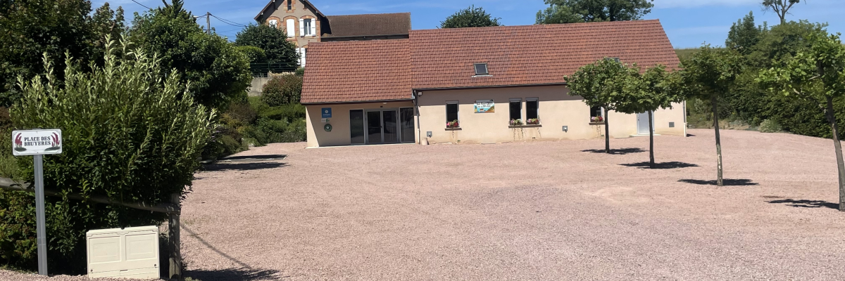 Parking avec gravier, bâtiments, arbres et panneau.