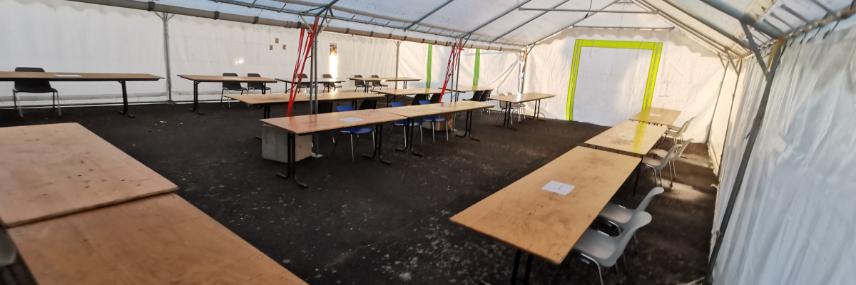 Salle sous tente avec tables, chaises et câbles suspendus.