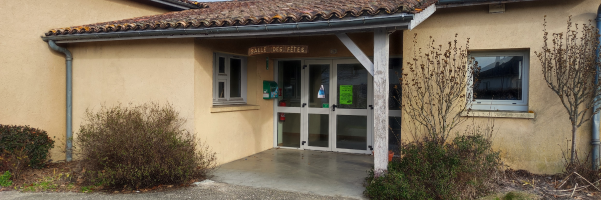 Bâtiment à un étage, enduit jaune, toit en tuile rouille, entrée avec porte en verre, allée gravillonnée.