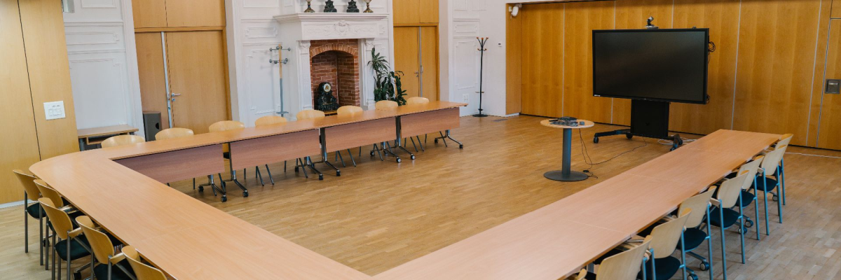 Salle de réunion avec grande table, chaises, écran et cheminée.