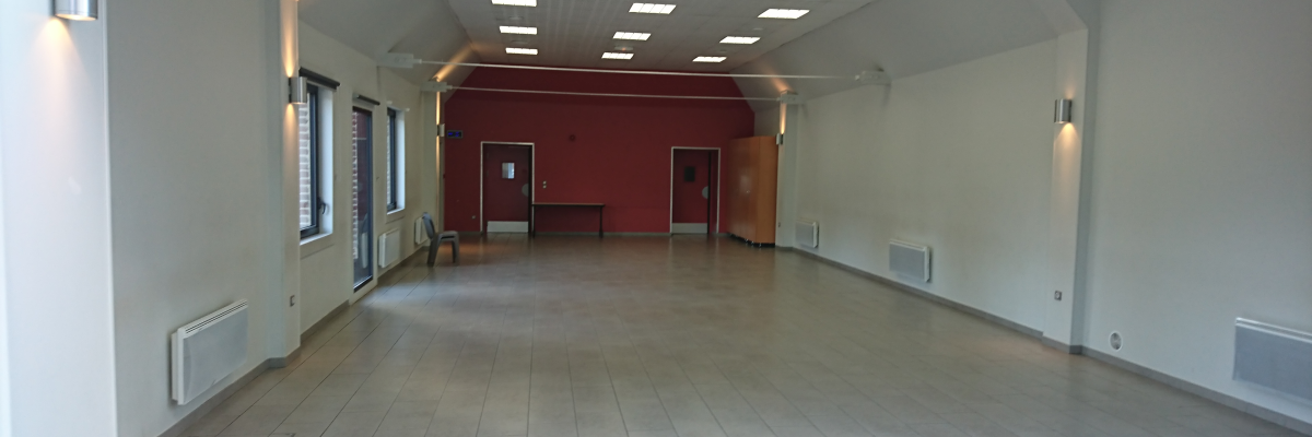 Pièce avec plafond haut, murs blancs, sol carrelé, portes, fenêtres, radiateurs et éclairages muraux.