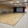 Salle avec plancher en bois, scène, projecteurs, murs blancs et carrelage.