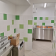Cuisine avec plaques de cuisson, four, réfrigérateur, étagères et carrelage vert et blanc.