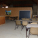 Salle avec tables, chaises, bar en bois, mur en OSB, porte métallique, fenêtres.