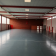 Salle spacieuse avec sol noir, murs rouges et blancs, portes, fenêtres et quelques équipements sportifs.