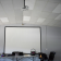 Salle avec écran, vidéo projecteur suspendu, table, chaises et matériel divers.