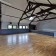 Salle avec plancher en bois, murs bleus, fenêtres, porte, escalier et poutres apparentes.