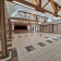 Salle spacieuse avec piliers en bois, sol carrelé, escaliers, portes vitrées et plafond haut.