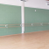 Salle avec barres de danse, mur vert, parquet, porte, extincteur et ventilateur.