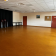 Salle avec parquet, chaises empilées, table, porte rouge, tableau d'affichage et rideau noir.