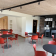 Salle avec tables rondes, chaises rouges, cuisine et projecteur.