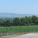 Stade de football avec piste d'athlétisme, parking et vue sur les montagnes.