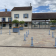 Bâtiment avec toits en tuiles, fenêtres bleues, antenne, pots de fleurs, poteaux et sol pavé.