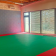 Salle avec tapis vert, murs gris, fenêtres et porte.