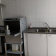 Cuisine avec plaque de cuisson, hotte, lave-vaisselle, évier, robinet et étagères.