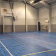 Salle de sport avec panier de basket, filet, échelle et sol bleu.
