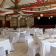 Salle avec tables, chaises, nappes, verres, vaisselle et décorations suspendues.