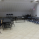 Salle avec tables, chaises, projecteur, trépied et climatiseurs.