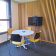 Table ronde avec chaises, téléviseur sur support, mur à rayures verticales.