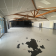 Salle vide avec sol blanc, poutres apparentes, portes et taches noires au sol.