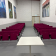 Salle avec rangées de chaises, table au centre, tableaux aux murs, porte.