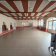 Salle vide avec sol carrelé, plafond à poutres apparentes, portes et fenêtres.
