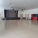 Salle spacieuse avec scène, écran, projecteurs, portes et comptoir rouge.