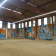 Atelier avec graffitis muraux, sol en béton, toit métallique, fenêtres.