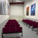 Salle avec rangées de chaises, tableaux aux murs, porte au fond.