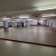 Grande salle vide avec éclairage au plafond, murs blancs avec bande rouge, sol carrelé.